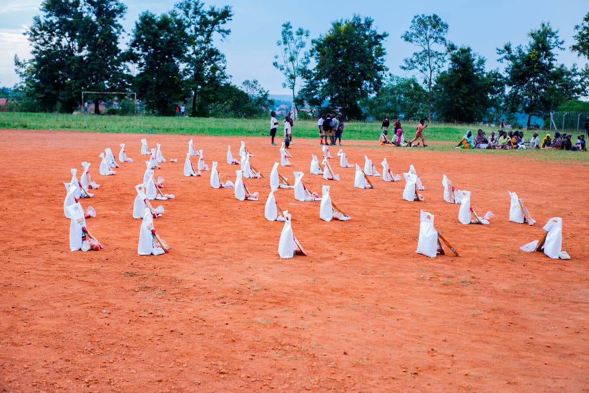 Rows of white food-pack sacks set out across a red-earth field before an HCIU distribution begins